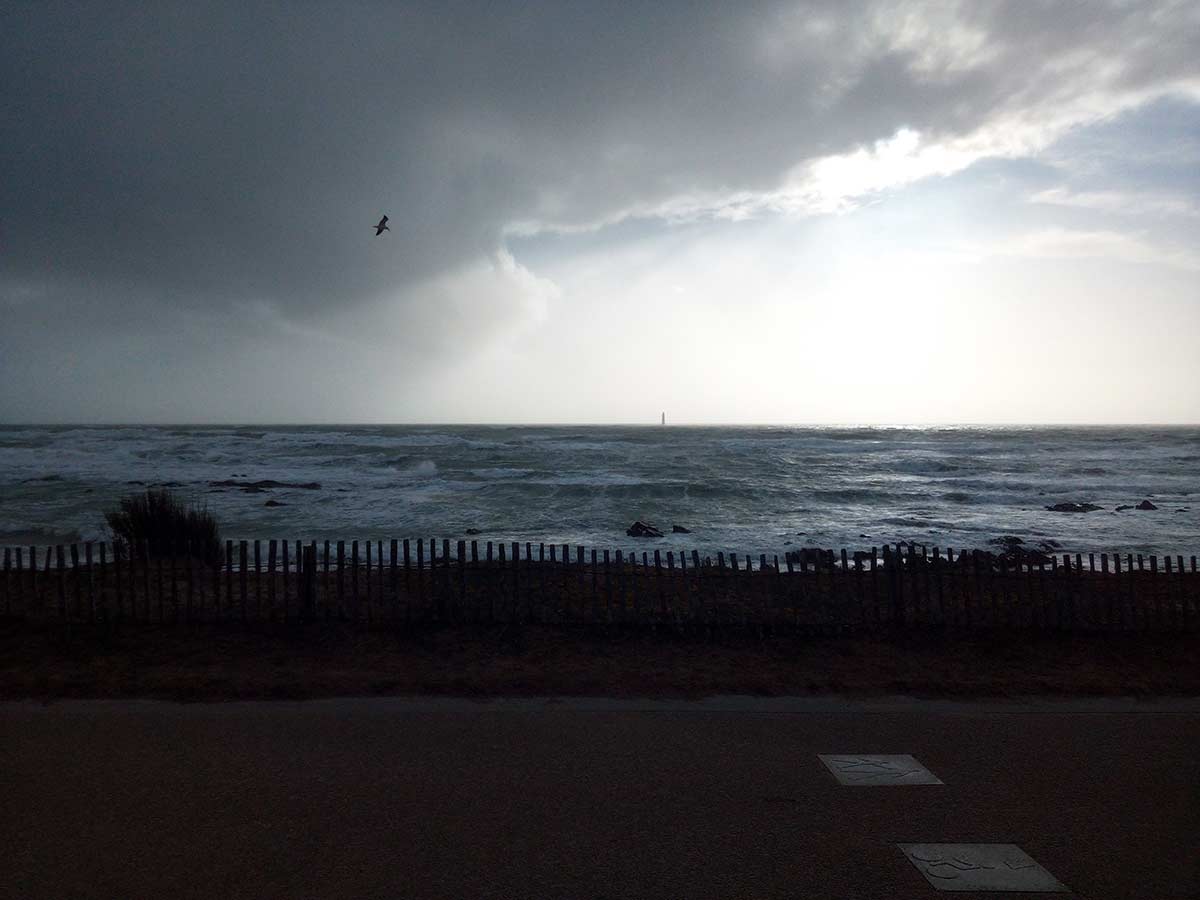 Stormy day, white waves, clouds, lighhouse and bird in Les Sables d'Olonne