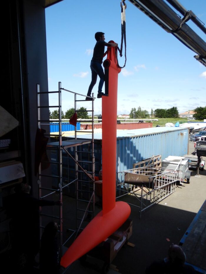 A qualified worker has one foot on top of a scaffolding and the other one on top of the kill of the Open60 AAL which is dismantled
