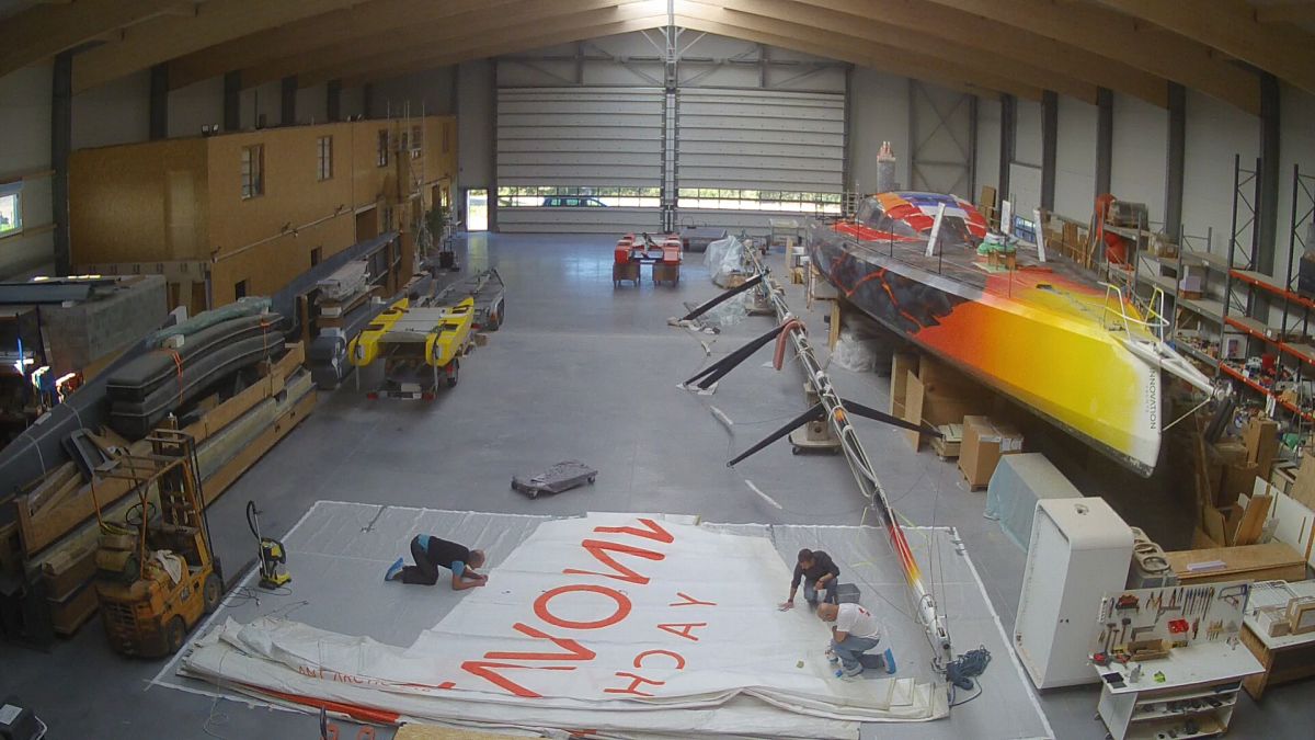 Three members of the team are working on the main sail on the floor of the shipyard