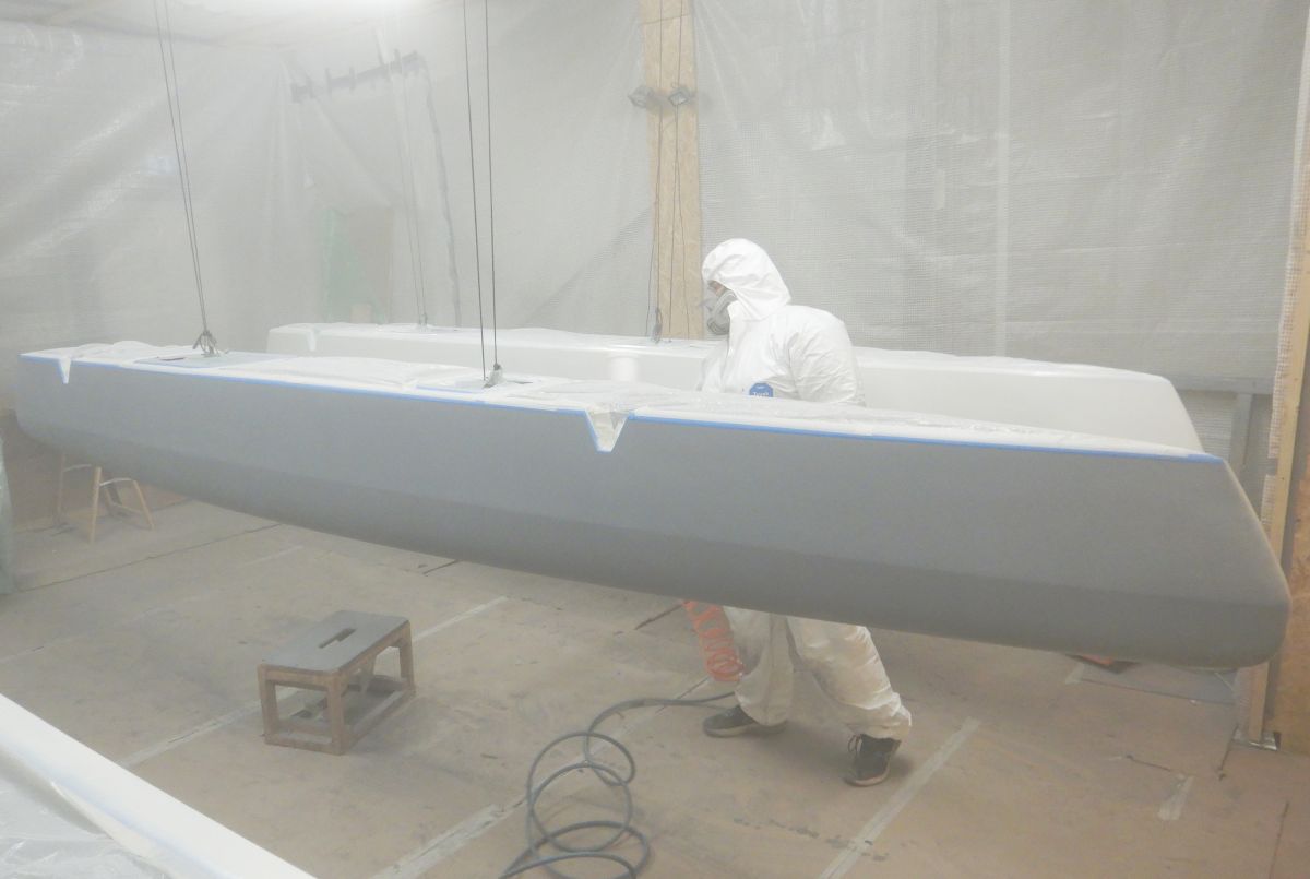 Ein Teammitglied in einem Overall lackiert den Rumpf eines Volcat16 mit einer Spritzpistole in der Werkstatt