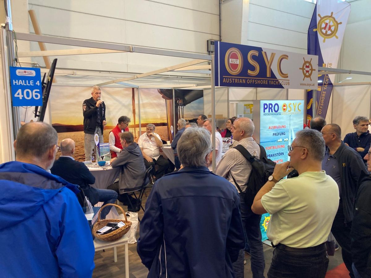Norbert is speaking on the stage of OSYC booth at Austrian Boat Show with people carefully listening to him