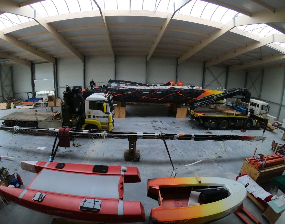 Im Inneren der Werkstatt, im Hintergrund die Steuerbordseite der Open60AAL, davor Lastwagen mit Kränen, sowie der Mast, die Volcat16 und die Lava330 direkt davor.