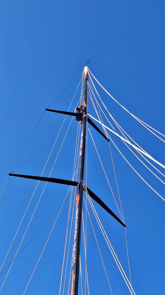 A team member is climbing the mast, going up to the highest part, to adjust the rigging.