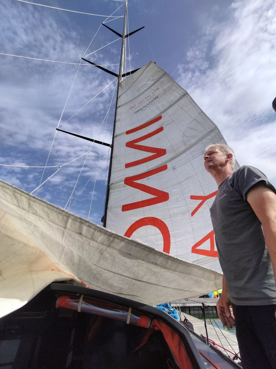 Norbert is standing on the Open60AAL, staring at what is coming, while the main sail is hoisting behind him. - ANT ARCTIC LAB