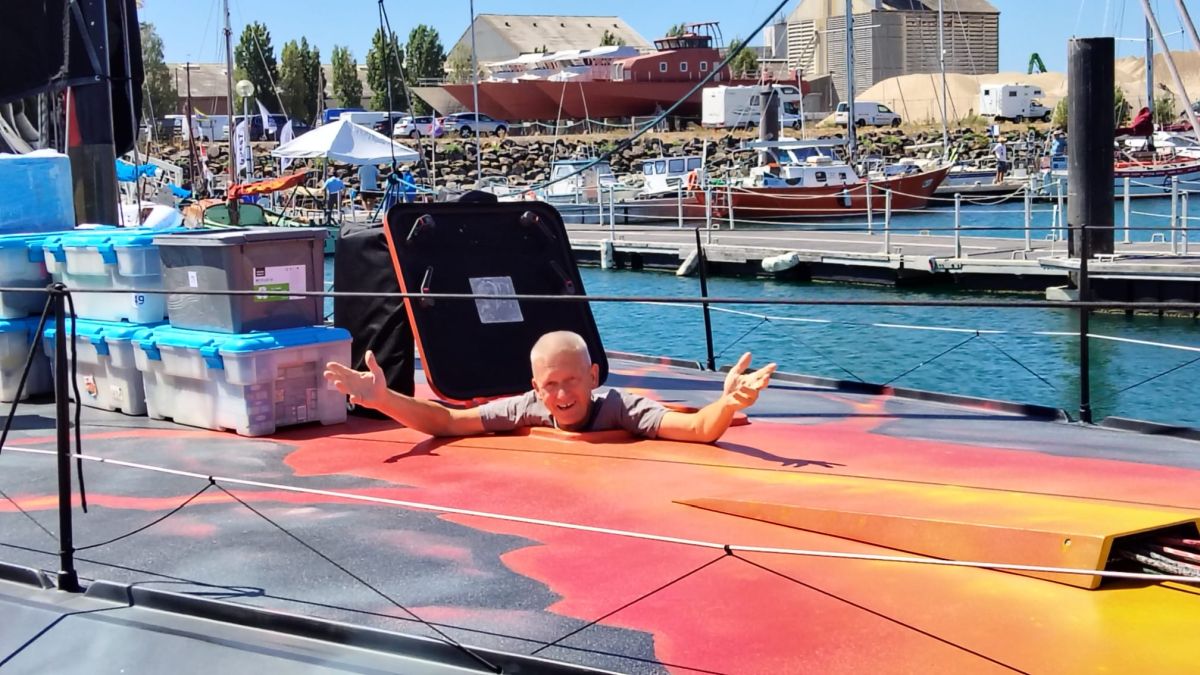 Norbert pokes his head through the hatch from the sails compartment, his arms raised, next to the boxes of food that are to be loaded. - ANT ARCTIC LAB